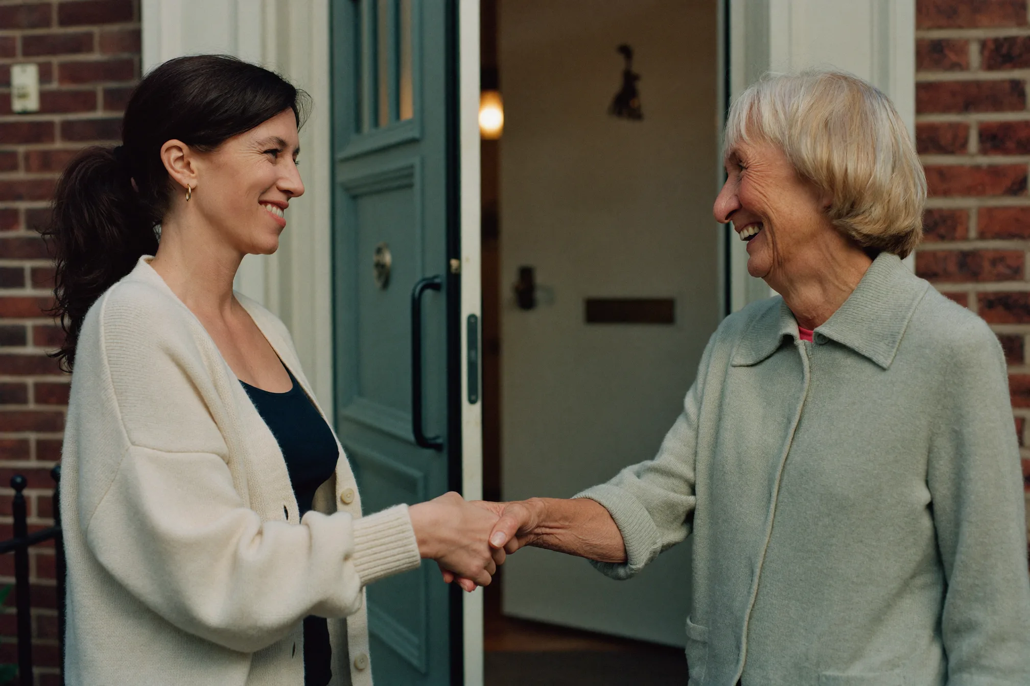 A support worker warmly shaking hands with a client at her front door